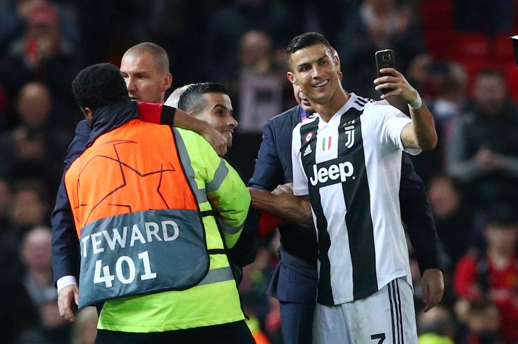 Juventus' Cristiano Ronaldo takes a selfie as stewards apprehend a pitch invader after the match.